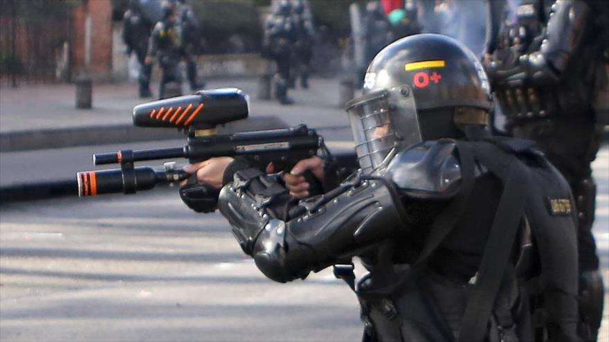 Policía colombiano apuntando con una escopeta calibre 12 a manifestantes.