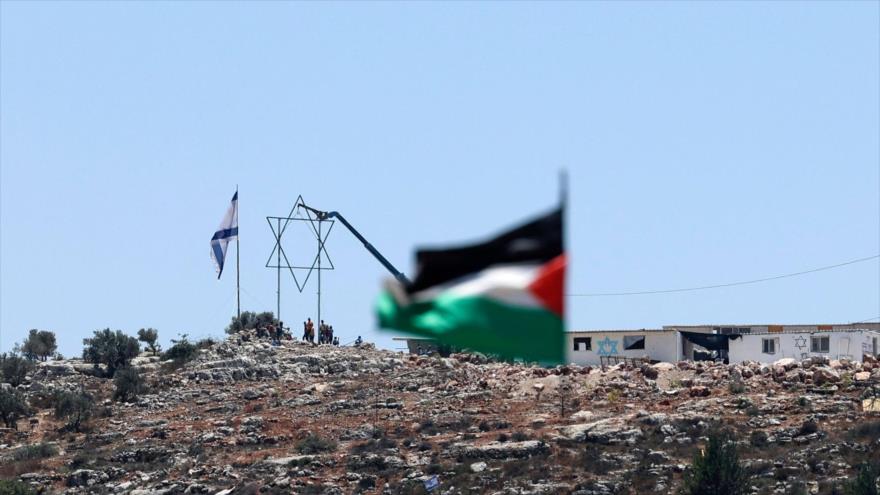 Bandera de Palestina frente al puesto de avanzada de colonos israelíes recién construido en la ocupada Cisjordania, 2 de julio de 2021. (Foto: AFP)