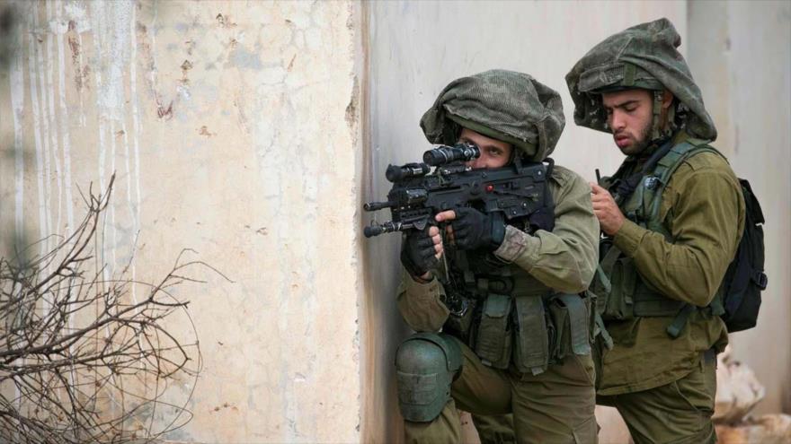 Dos soldados israelíes apuntando sus armas contra manifestantes palestinos en la Cisjordania ocupada.