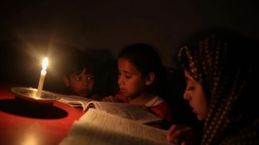 Niños palestinos leen un libro a la luz de las velas debido al corte de energía en el campamento de Jabalia en la ciudad de Gaza, 27 de junio de 2017.