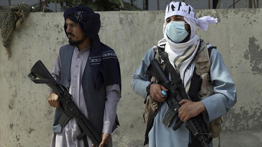Talibanes con armas estadounidenses montan guardia en la puerta principal que conduce al palacio presidencial en Kabul, 16 de agosto de 2021.