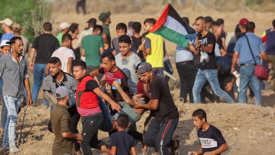 Manifestantes palestinos trasladan a un joven herido por los disparos de las fuerzas israelíes al este de Gaza, 21 de agosto de 2021. (Foto: AFP)
