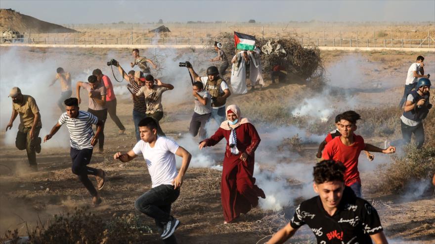 Los manifestantes y periodistas palestinos huyen de los gases lacrimógenos disparados por militares israelíes durante una protesta en Gaza, 25 de agosto de 2021. (Foto: AFP)