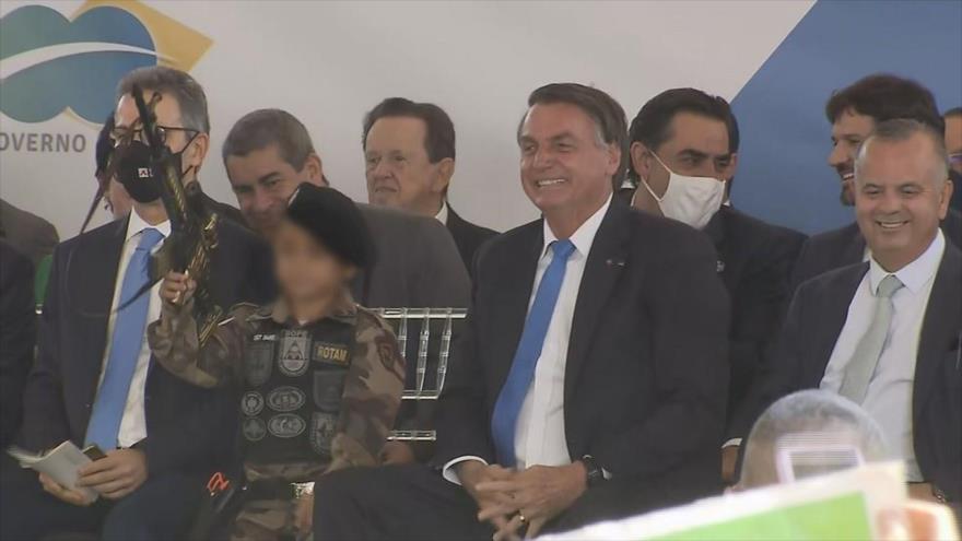 El presidente de Brasil, Jair Bolsonaro, obliga a un niño a hacer flexiones en la tarima con un fusil de juguete, 30 de septiembre de 2021.