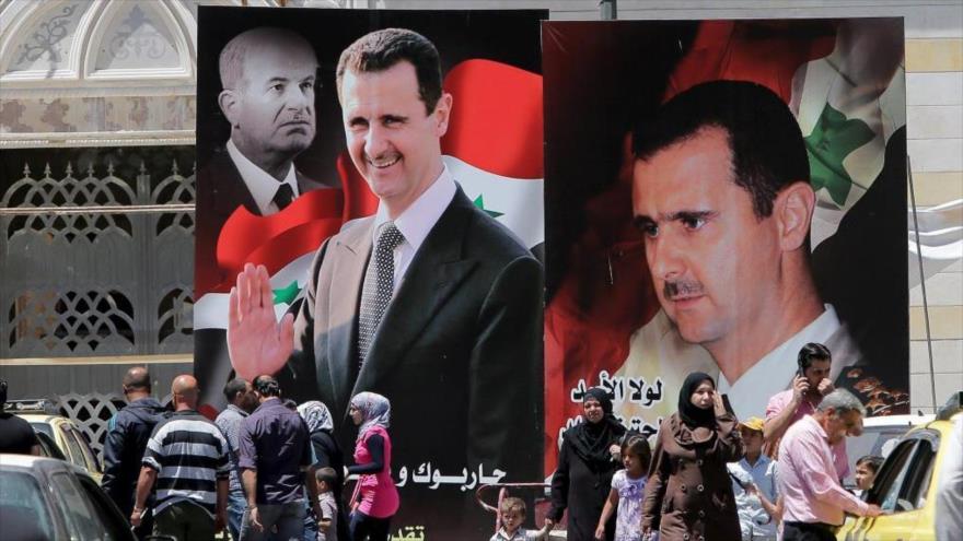 Sirios pasean por una calle en la que se han desplegado carteles con el retrato del presidente, Bashar al-Asad, en Damasco. (Foto: AFP)