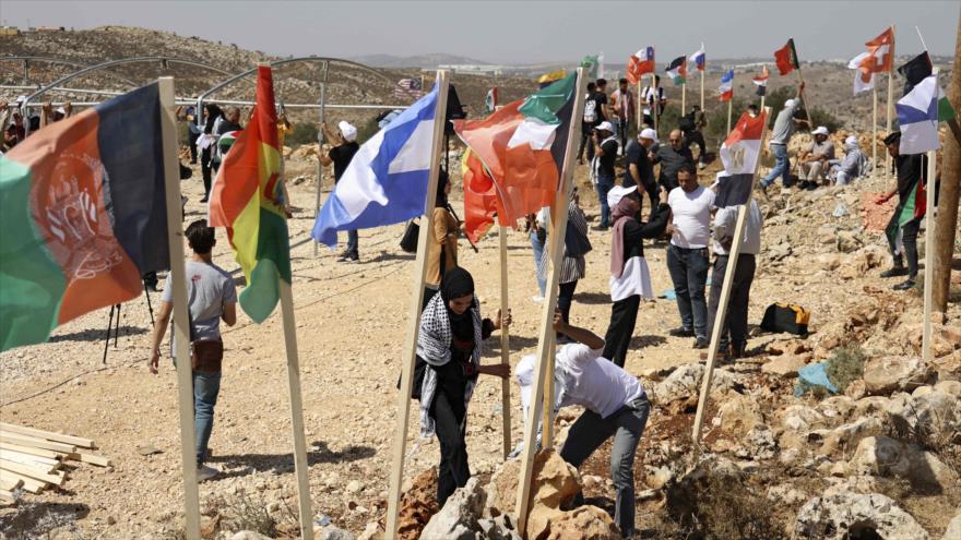 Activistas palestinos izan banderas de países que se oponen a asentamientos ilegales israelíes cerca de Salfit, 20 de septiembre de 2021. (Foto: AFP)