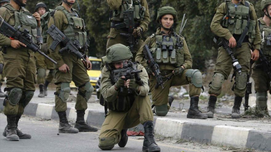 Soldado israelí apunta a un grupo de manifestantes palestinos con un rifli M-16. 