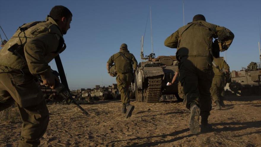 Soldados israelíes corren para refugiarse bajo un vehículo blindado durante un ataque con misiles lanzado desde Gaza, 15 de mayo de 2021. (Foto: AP)