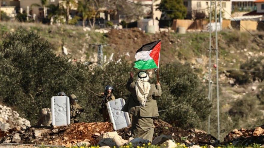 Un palestino levanta bandera nacional ante israelíes en una protesta contra expropiación de tierras por Israel en Cisjordania, 21 de enero de 2022.