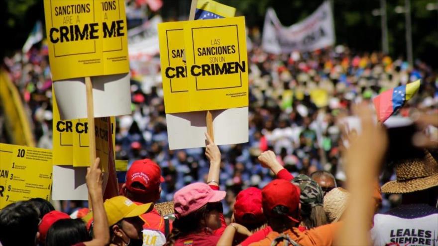 Trabajadores venezolanos sostienen pancartas que dicen: “Las sanciones son un crimen”, durante una marcha en Caracas, 1 de mayo de 2022.