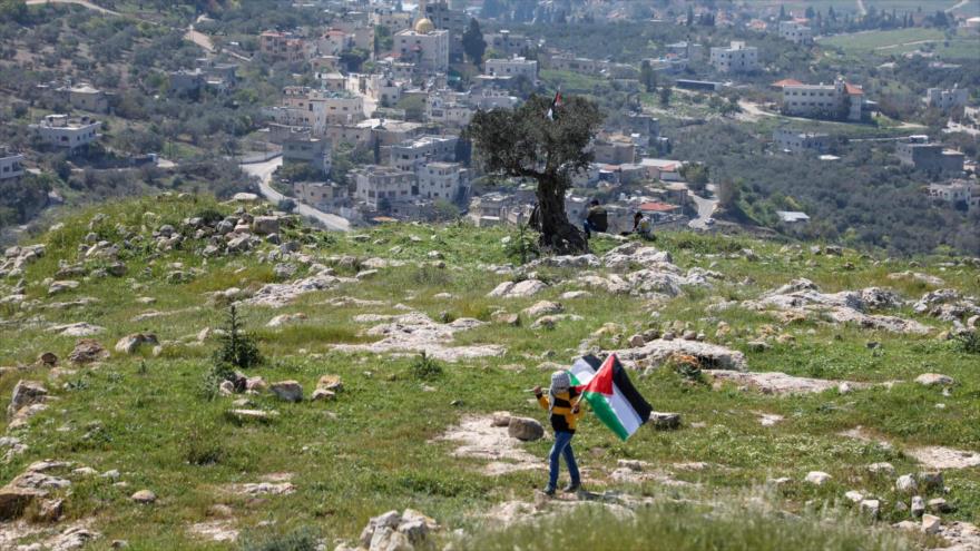 Un hombre porta la bandera palestina durante una protesta contra la expansión de colonias israelíes cerca de Nablus, en el norte de Cisjordania, 29 de marzo de 2021. (Foto: AFP)
