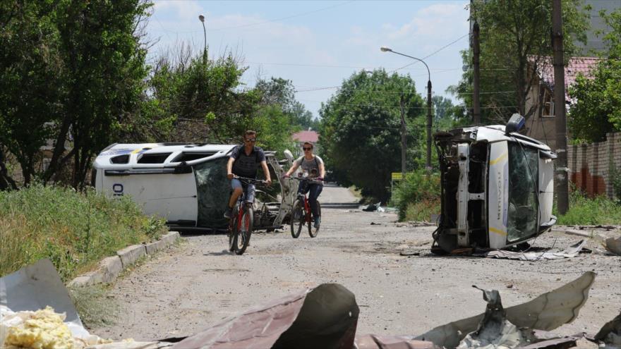 Residentes en bicicleta pasan junto a un coche destruido en Lisichansk, 4 de julio de 2022. (Foto: Xinhua)