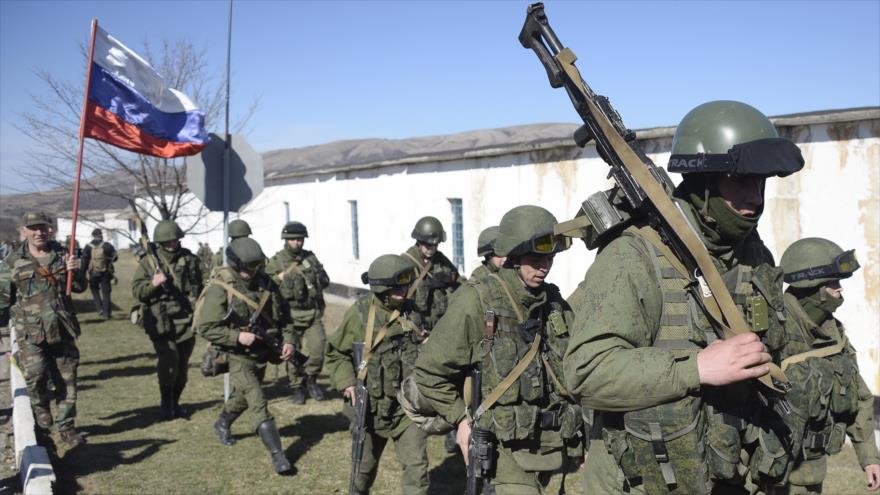 Un militar con una bandera rusa, junto con otros militares, intentan bloquear la frontera ucraniana. (Foto: AFP)