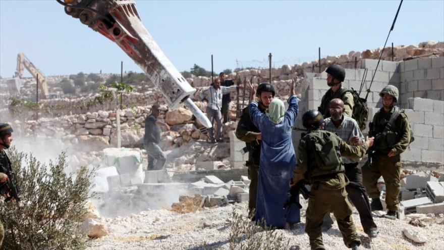 Agentes israelíes hacen guardia mientras una maquinaría israelí destruye una estructura palestina cerca de Al-Jalil (Hebrón). (Foto: AFP)
