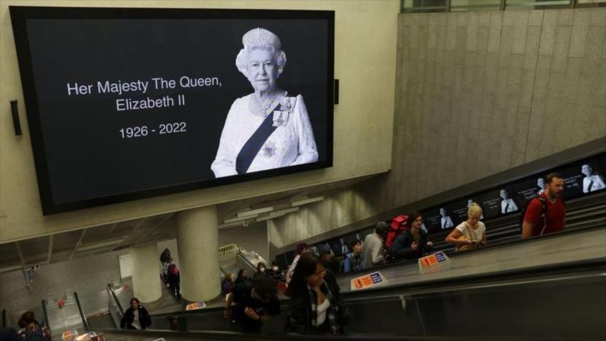 Los viajeros pasan por debajo de una imagen de homenaje a la reina Isabel II en una estación de tren en Londres, 10 de septiembre de 2022. (Foto: AFP)