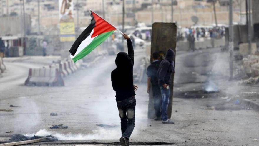 Un palestino levanta la bandera nacional en los enfrentamientos con las fuerzas israelíes en la ocupada Cisjordania.