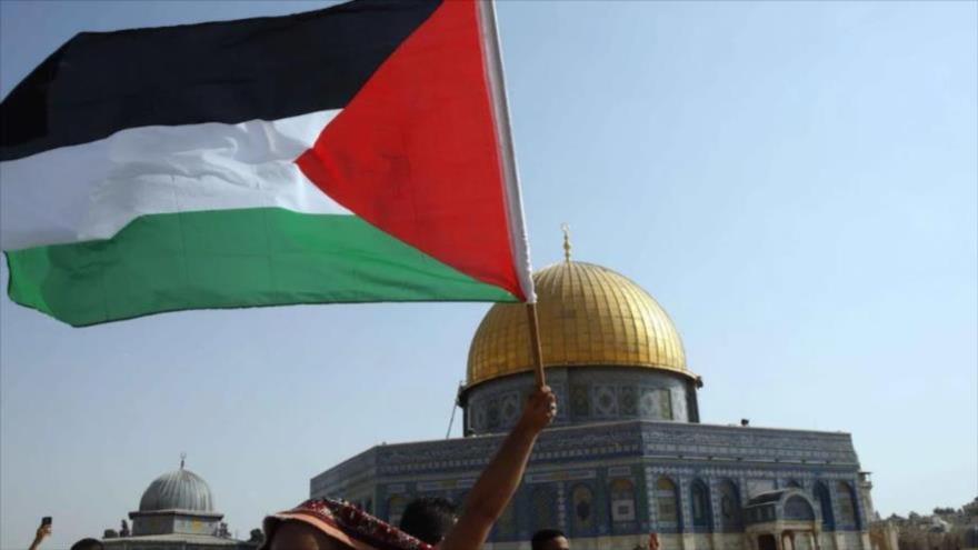 Palestinos ondean su bandera nacional frente a la Cúpula de la Roca en la Explanada de la Mezquita Al-Aqsa, en Al-Quds.