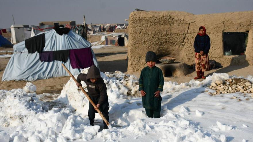 Niños afganos desplazados palean nieve cerca de sus tiendas durante un frío día de invierno en la provincia de Balj, 17 de enero de 2023. (Foto: AFP)