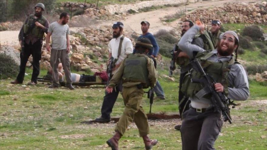Colono armado israelí lanza piedras contra los palestinos ante los ojos de los extremistas y fuerzas militares de Israel.