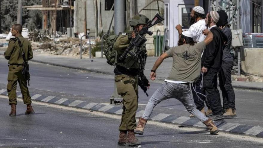 Soldados israelíes junto a colonos que arrojan piedras a los palestinos durante un enfrentamiento en la ciudad de Huwara en Cisjordania ocupada, 13 de octubre de 2022.