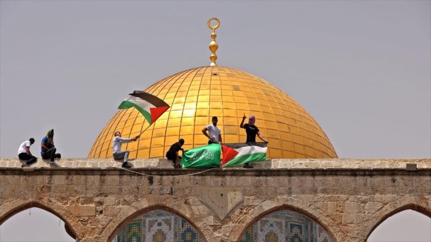 Palestinos izan banderas nacionales y de HAMAS en el recinto de la Mezquita Al-Aqsa frente a la Cúpula de la Roca, 20 de julio de 2021. (Foto: Flash90)