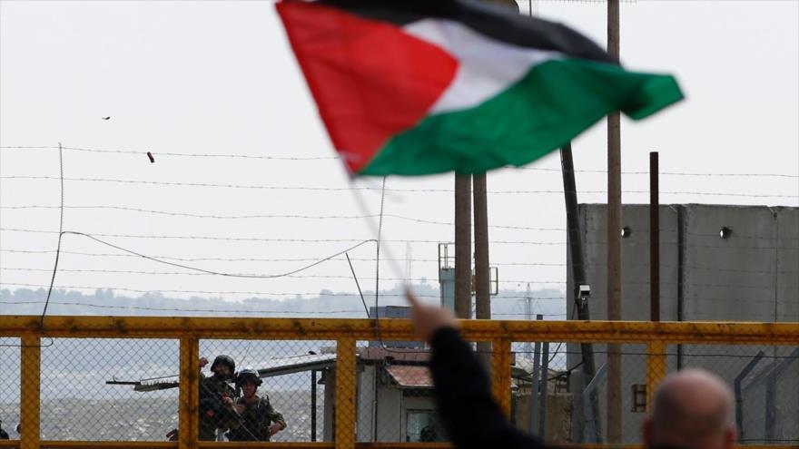 Un palestino ondea bandera nacional palestina frente a las fuerzas israelíes fuera de la prisión de Ofer, Cisjordania, 30 de marzo de 2016. (Foto: AFP)