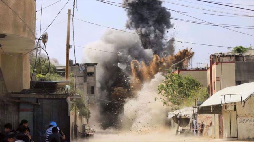 La gente se refugia detrás de un muro cuando un edificio en Beit Lahia, al norte de la Franja de Gaza, es atacado por Israel, 12 de mayo de 2023. (Foto: AFP)