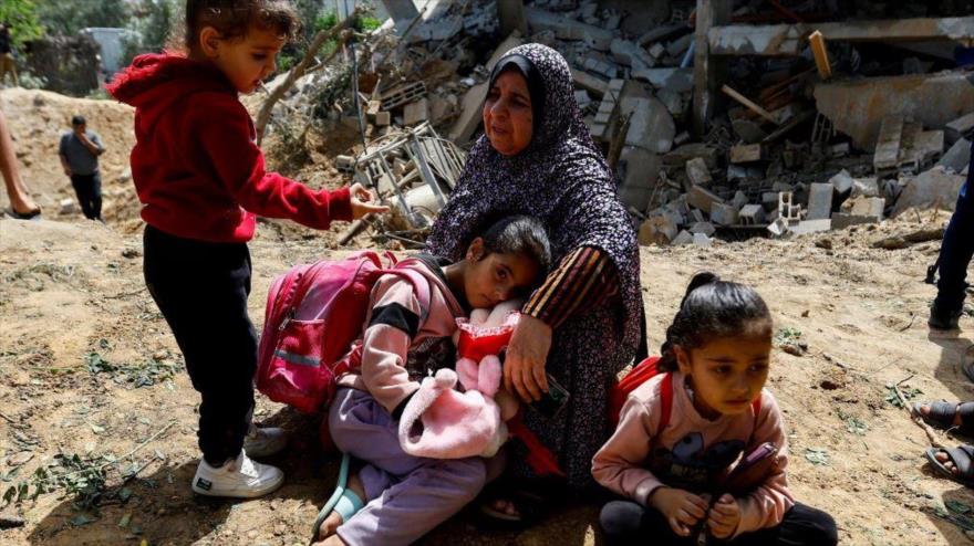 Mujer palestina y sus nietas se sientan junto a su casa derruida por los ataques aéreos israelíes, Gaza, 12 de mayo de 2023. (Foto: Reuters)