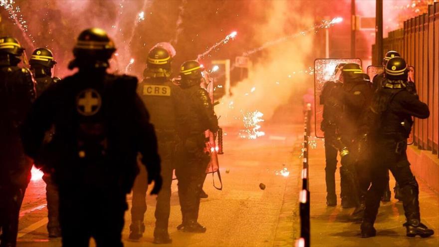 La Policía francesa permanece en posición mientras bengalas estallan durante las protestas en Nanterre, suburbio de París, 30 de junio de 2023.