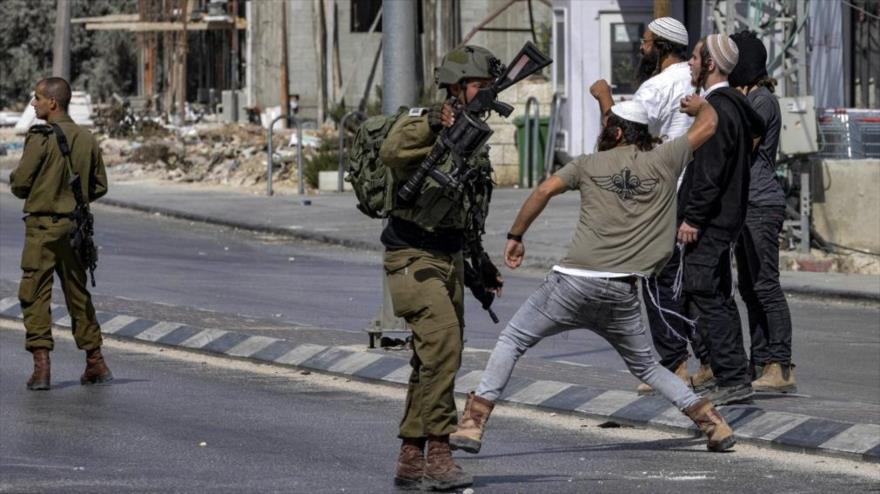 Colonos israelíes al lado de soldados lanzan piedras a los palestinos en la ciudad de Huwara en Cisjordania ocupada, 13 de octubre de 2022. (Foto: AFP)