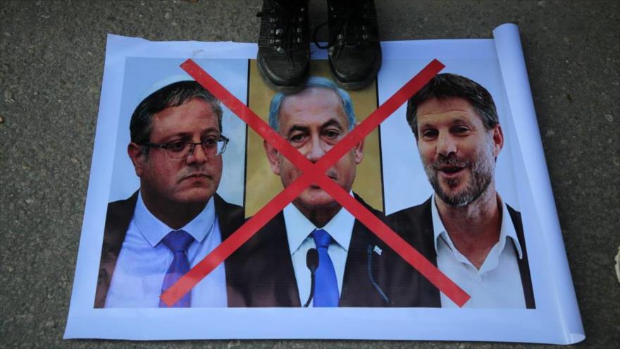 Pisotean foto del premier israelí, Benjamín Netanyahu (centro), y sus ministros, Itmar Ben-Gvir (izda.) y Bezalel Smotrich en una protesta en Gaza.