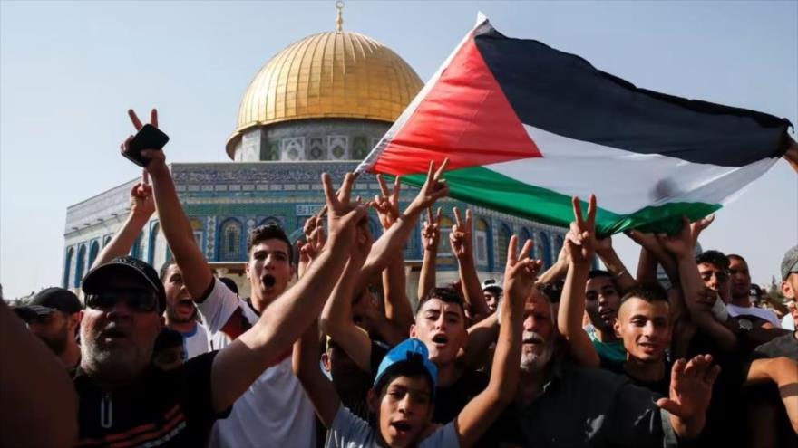 Palestinos ondean una bandera nacional y hacen el gesto de victoria frente a la Cúpula de la Roca en el recinto de la Mezquita Al-Aqsa, en Al-Quds. (Foto: AFP)