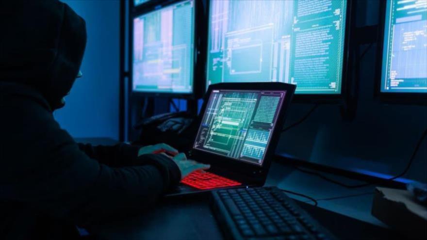 Una imagen representativa sobre un hacker con una máscara negra en una sala de servidores. 