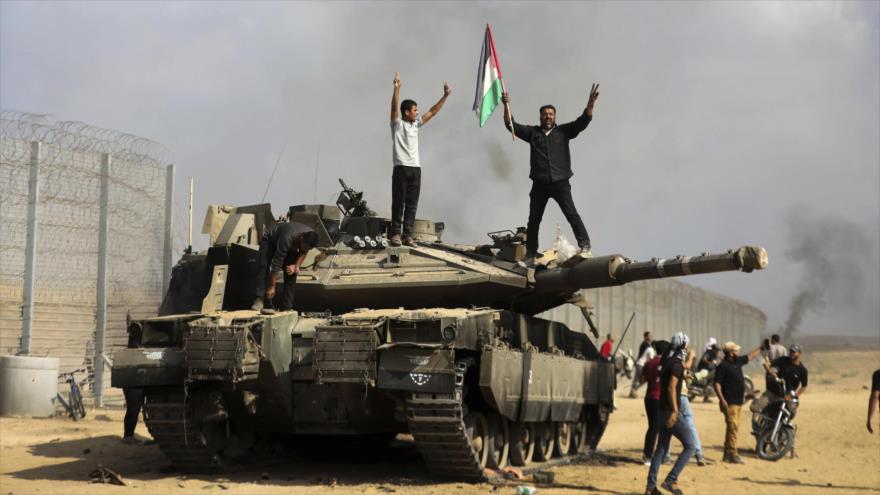 Los palestinos celebran junto a un tanque israelí destruido por HAMAS en la valla fronteriza con Gaza, al este de Jan Yunis, 7 de octubre de 2023. (Foto: AP)