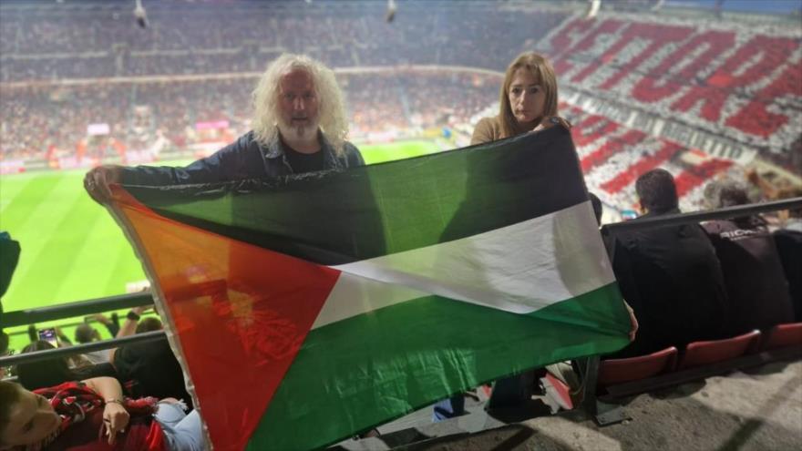 Eurodiputados Clare Daly (dcha.) y Mike Wallace portan una bandera palestina en un estadio de fútbol.