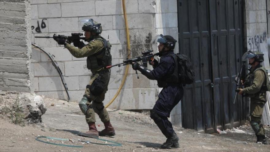 Soldados israelíes apuntan con sus armas a los palestinos en Beit Ummar, en la ciudad cisjordana de Al-Jalil (Hebrón).