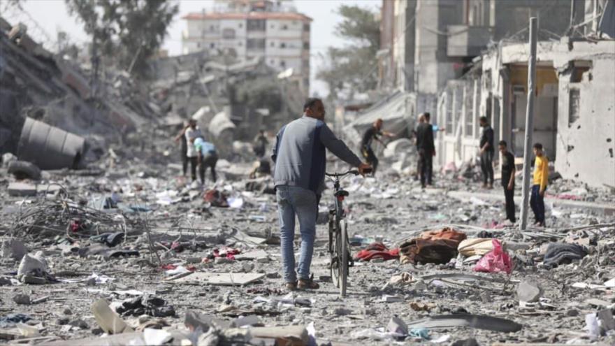 Palestinos caminan junto a los edificios destruidos por un bombardeo israelí en Al-Zahra, en las afueras de la ciudad de Gaza. Foto: AP)