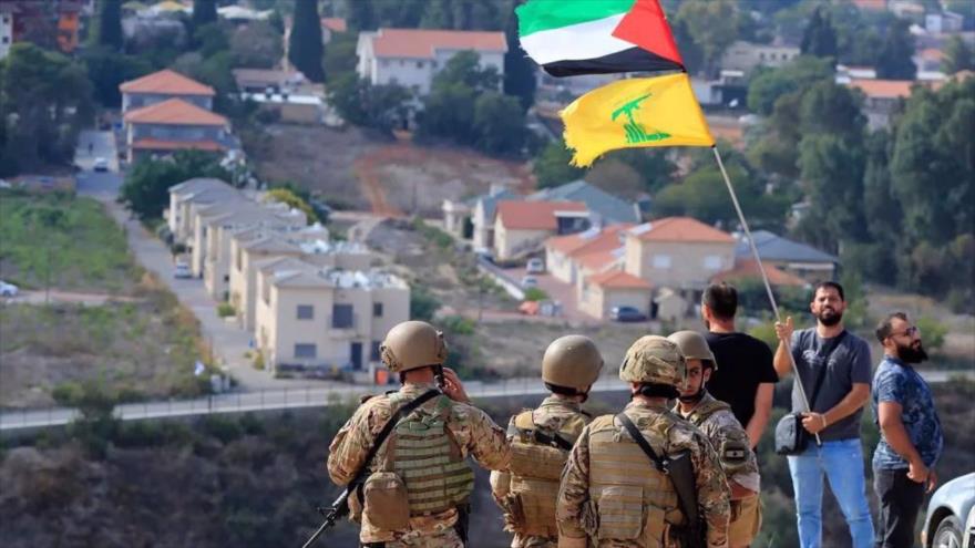 Soldados libaneses se encuentran en una colina que domina la ciudad israelí de Metula mientras un hombre ondea las banderas palestinas y de Hezbolá, Líbano, 9 de octubre de 2023. (Foto: AP)