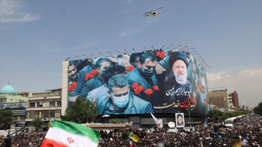 Los dolientes se reúnen bajo un gran cartel que conmemora al presidente mártir iraní Seyed Ebrahim Raisi en Teherán, 22 de mayo de 2024.