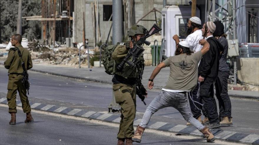 Soldados israelíes observan cómo colonos israelíes lanzan piedras a palestinos en Cisjordania, 13 de octubre de 2022. (Foto: AFP)