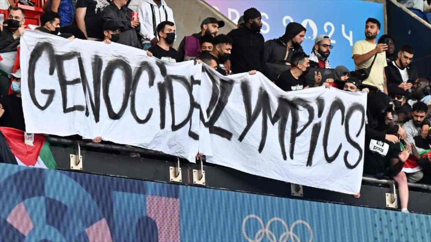 Manifestantes sostienen una pancarta que dice Olimpiadas del Genocidio, durante el partido de fútbol masculino entre Israel y Paraguay en el estadio París ,27 de julio de 2024.