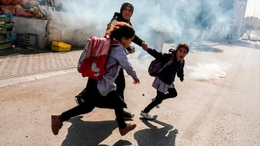 Una mujer palestina y dos colegialas intentan huir de los gases lacrimógenos lanzados por las fuerzas israelíes en Cisjordania. (Foto: AFP)