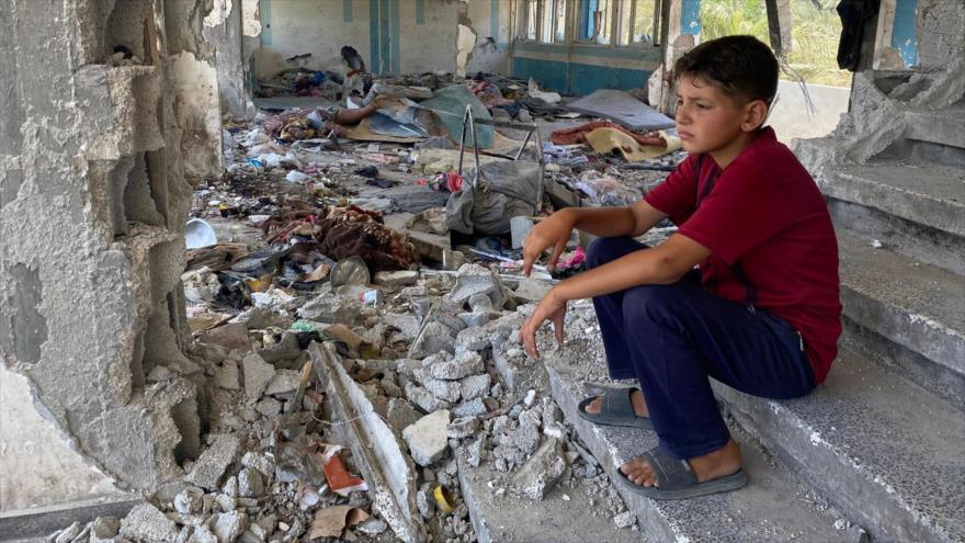 Un niño sentado entre los escombros de una escuela destruida por Israel.