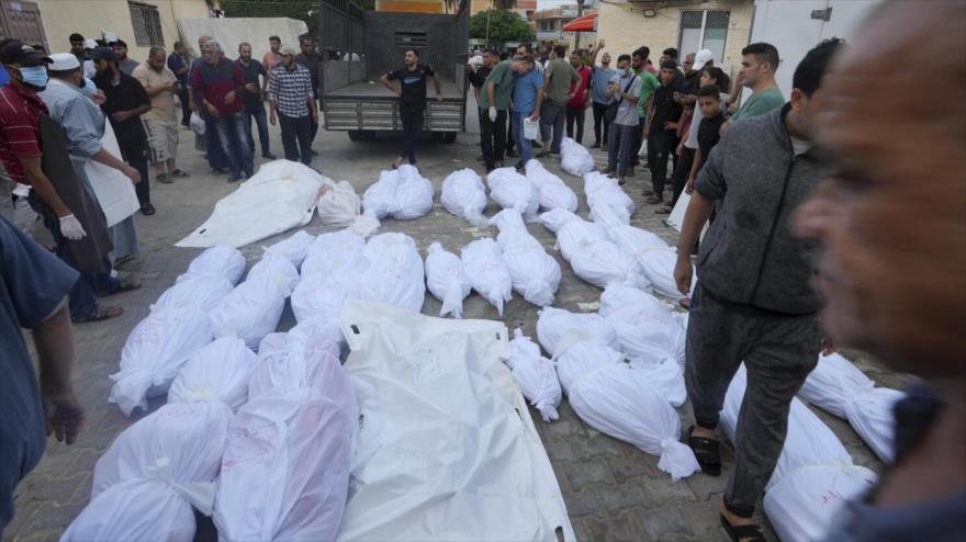 Palestinos de pie junto a cadáveres de personas que murieron por bombardeos israelíes en Gaza, 24 de octubre de 2023. (Foto: AP)