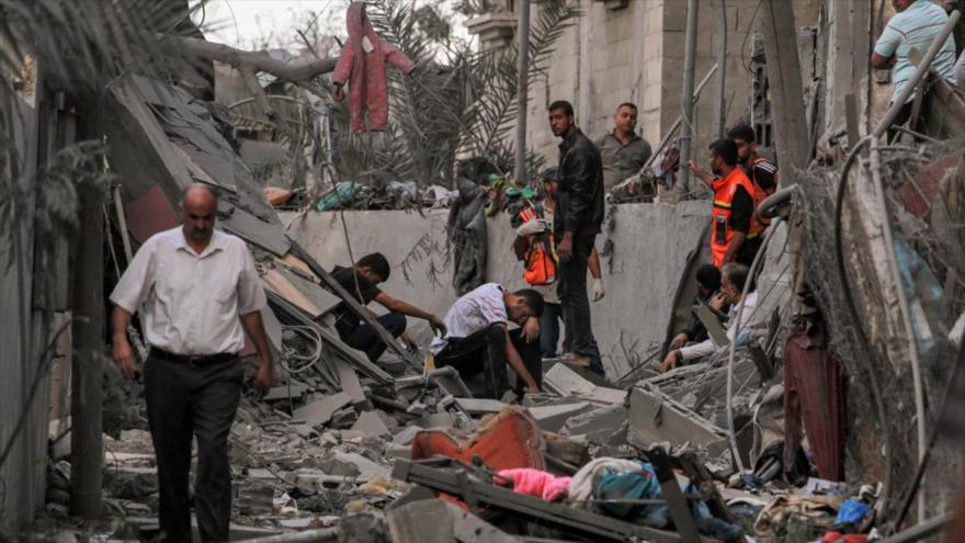 Rescatistas de Defensa Civil Palestina y otras personas permanecen entre escombros junto a un edificio derrumbado en Jan Yunis, en sur de Gaza.