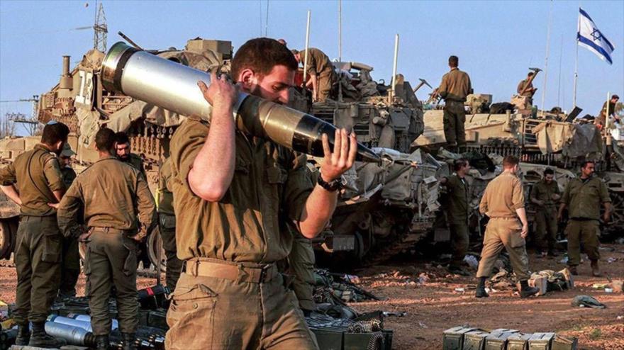 Un soldado israelí lleva un proyectil pesado junto a tanques desplegados a lo largo de la frontera con Gaza, 31 de diciembre de 2023. (Foto: AFP)