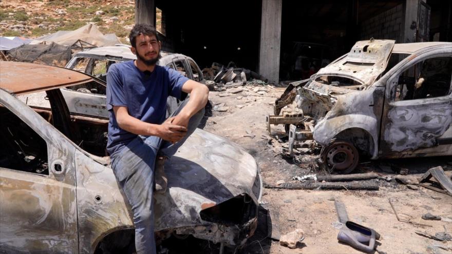 Un palestino se sienta sobre uno de automóviles calcinados en incendio de su casa y su taller durante ataques de colonos israelíes. 