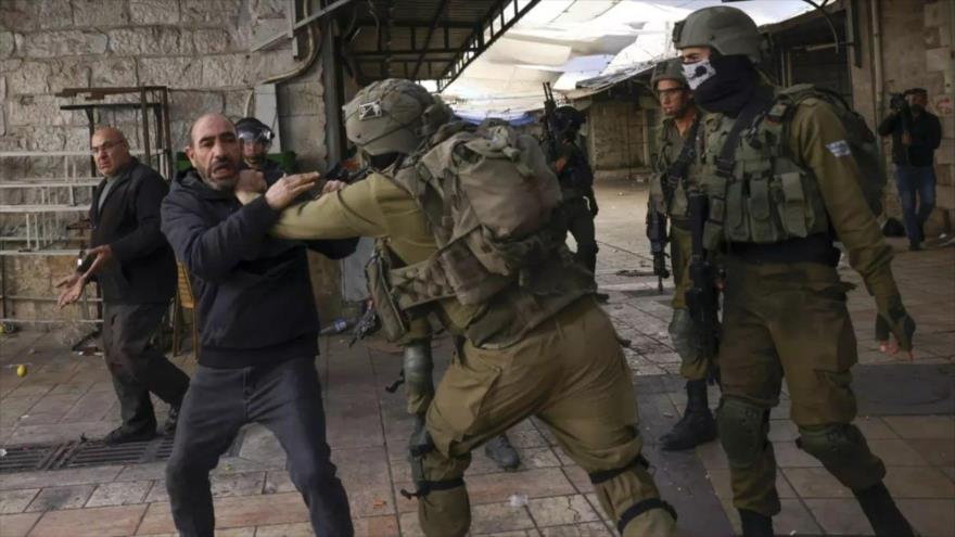 Militares israelíes detienen a un hombre palestino mientras los colonos judíos marchan en la ciudad ocupada de Hebrón, en Cisjordania, 19 de noviembre de 2022. (Foto: AFP)