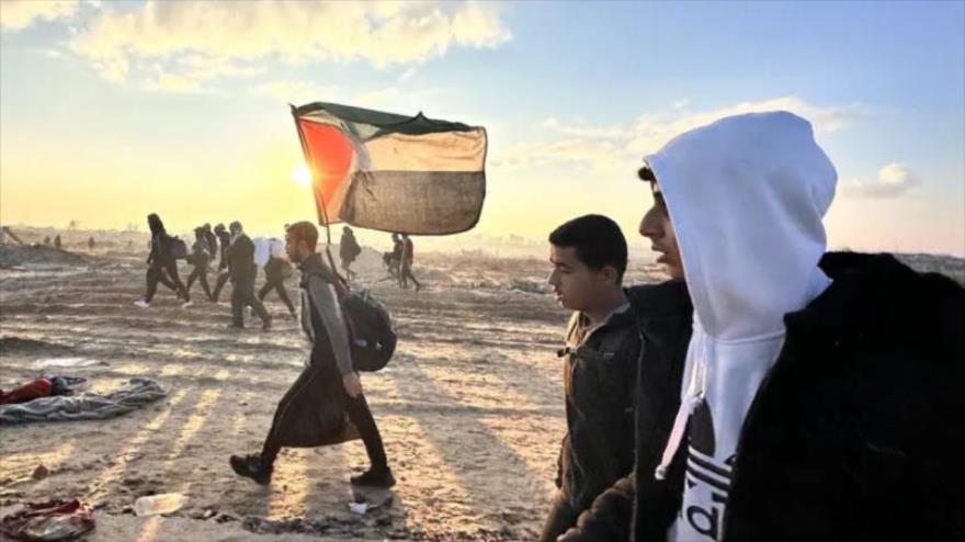 Un hombre con una bandera palestina camina junto a decenas de miles de personas que fueron desplazadas por la fuerza por las fuerzas israelíes al sur de Gaza, mientras regresan a sus hogares en el norte del enclave, 27 de enero de 2025. (Foto: Anadolu)