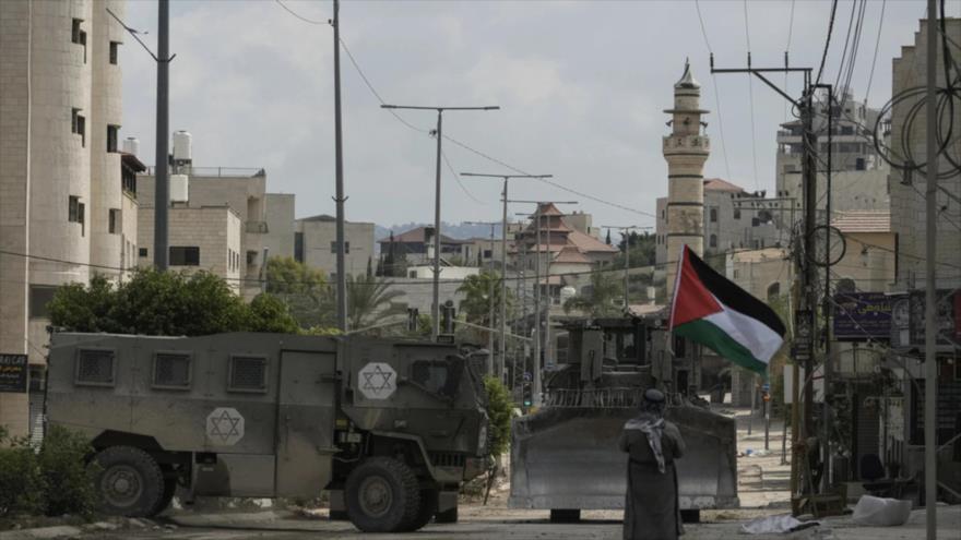 Un hombre enarbola una bandera de Palestina ante vehículos blindados del ejército israelí durante su redada en Tulkarem, Cisjordania, 27 de enero de 2025.